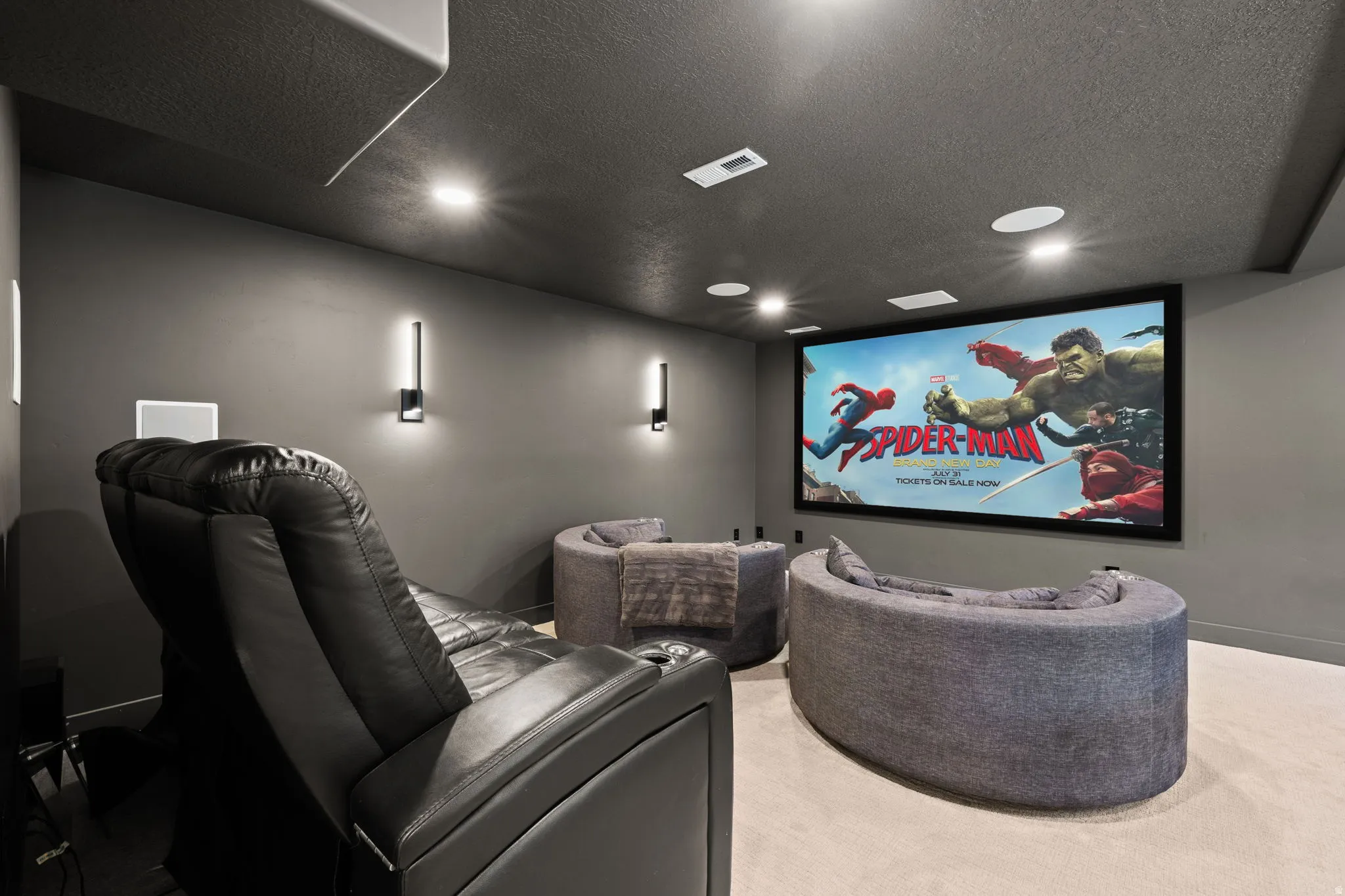 Dedicated media room featuring a large projection screen, recessed ceiling lighting, wall-mounted sconces, and in-ceiling speakers