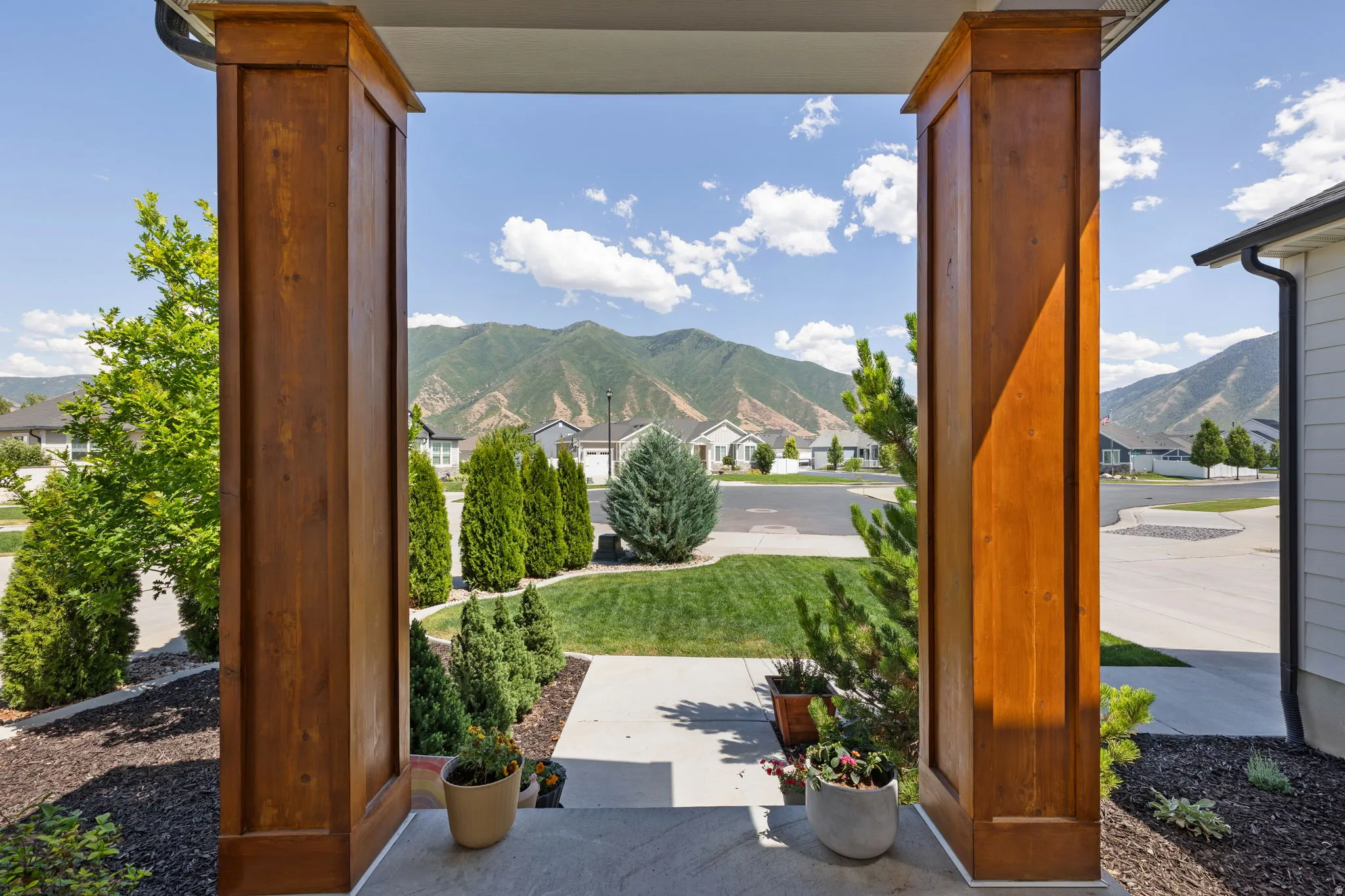 Covered porch entry featuring wood-finish support columns, a concrete walkway, and a landscaped front yard with decorative plantings