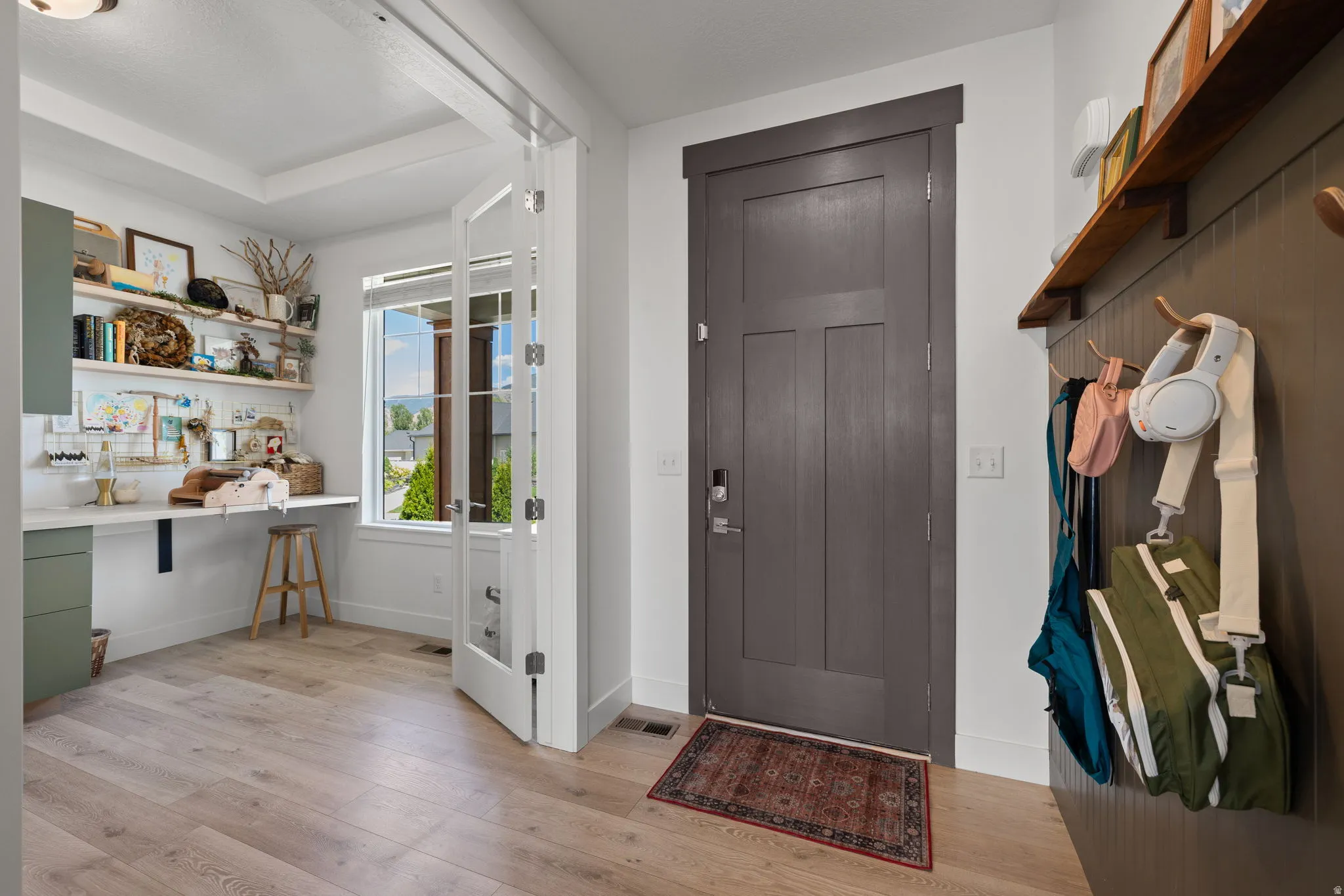 Entryway featuring a solid wood-panel door, light wood-finish flooring, and a built-in board-and-batten coat rack with a wood shelf
