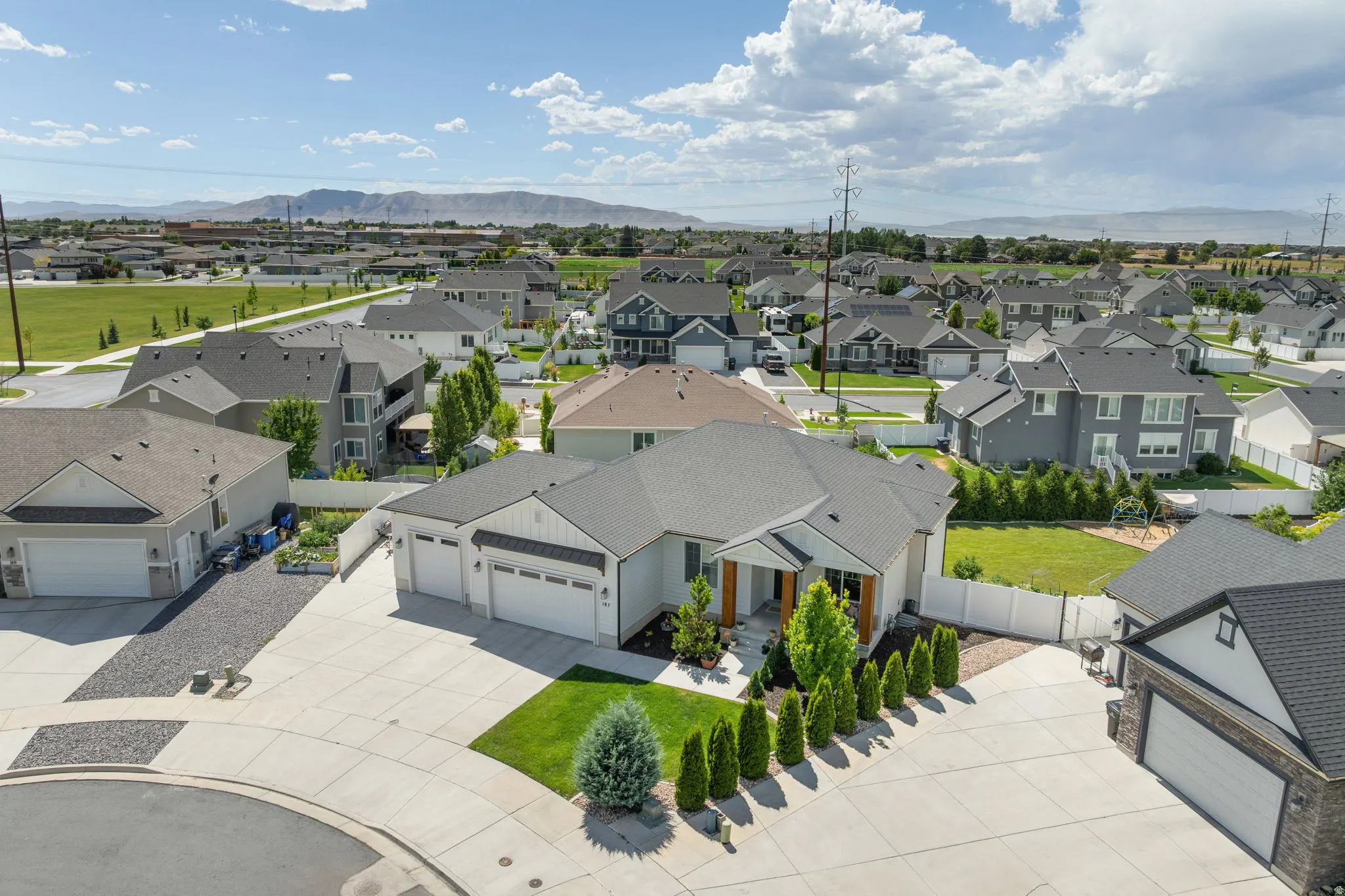 Contemporary ranch-style home featuring a three-car garage, concrete driveway, and a landscaped front yard with mature trees and shrubs