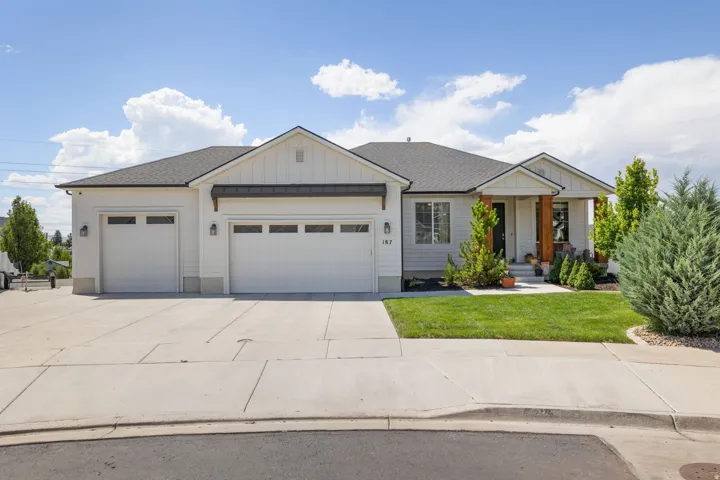 Contemporary ranch-style exterior featuring white siding, a dark gray roof, a spacious two-car garage, an inviting covered entry with wood-clad columns, and a landscaped front yard with mature shrubbery and green lawn