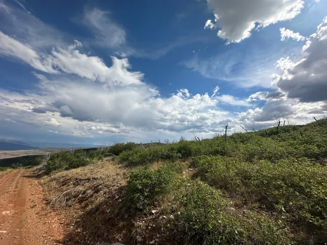Expansive undeveloped land featuring a red earth road, natural shrubbery, and distant mountain ranges
