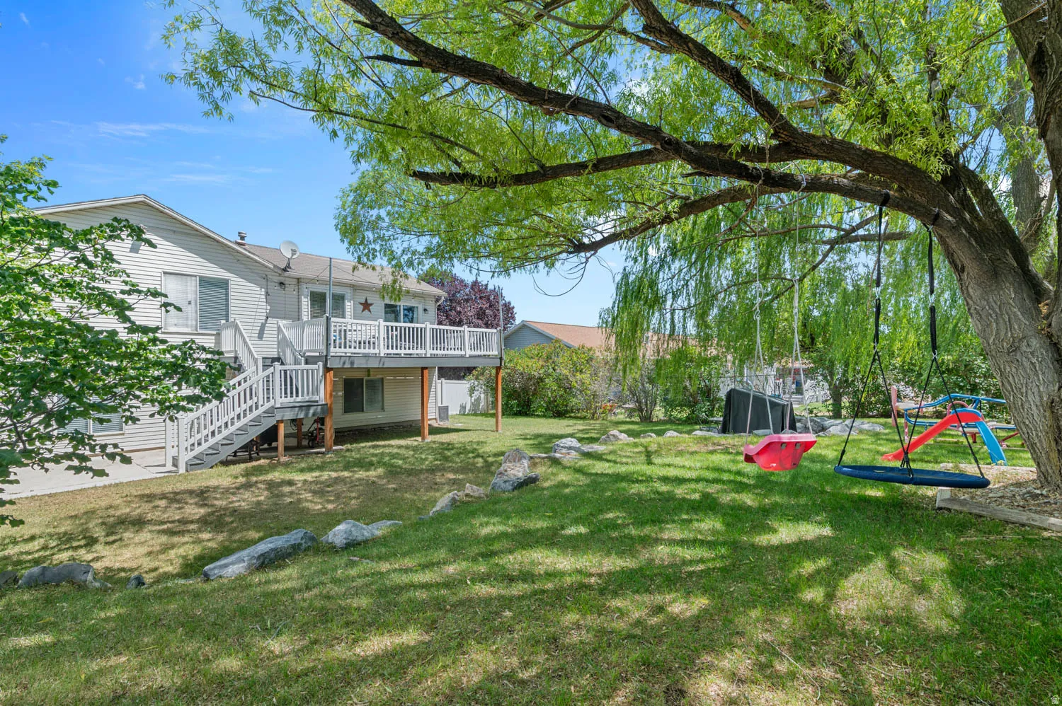 Spacious backyard featuring a multi-level deck with white railings, a lower-level concrete patio, a mature shade tree, and a grassy lawn