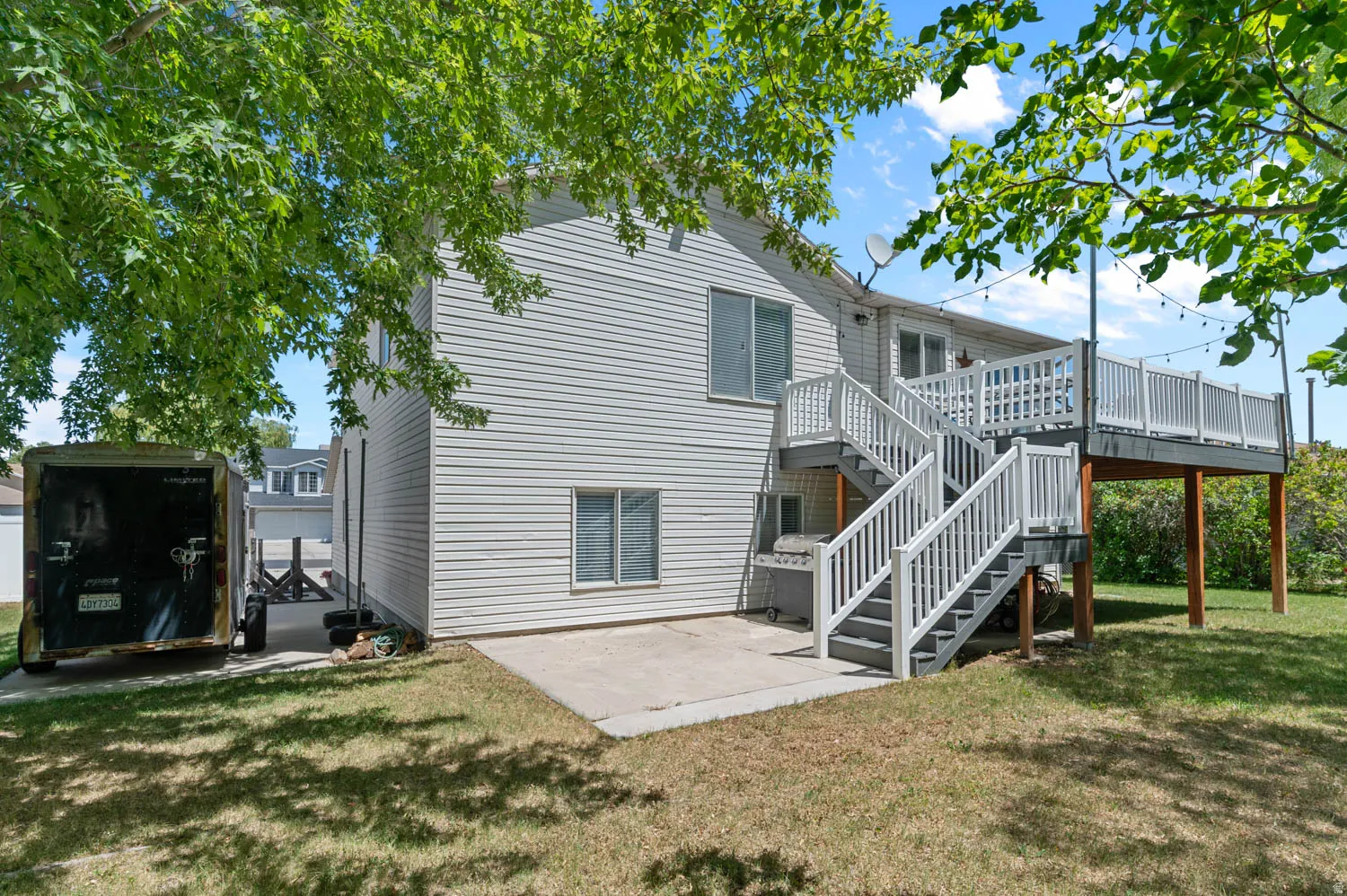Rear exterior featuring a multi-level deck with white railings and gray stairs, ground-level concrete patio, and a grass lawn