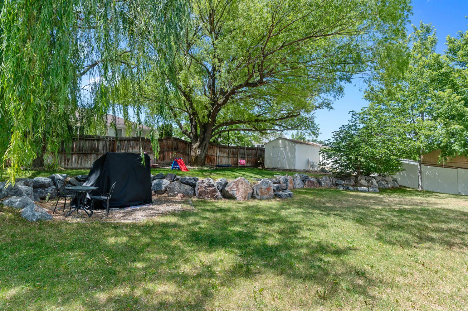 Expansive backyard featuring a large tree providing shade and a rock retaining wall