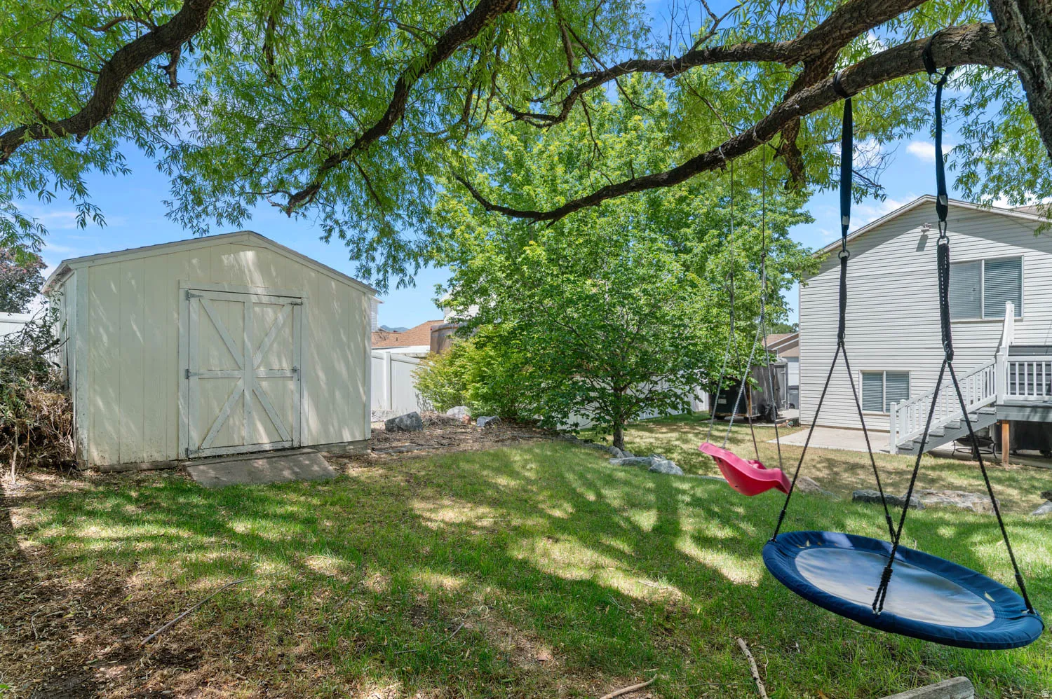 Expansive backyard featuring a lush lawn, mature trees, and a detached storage shed with double doors