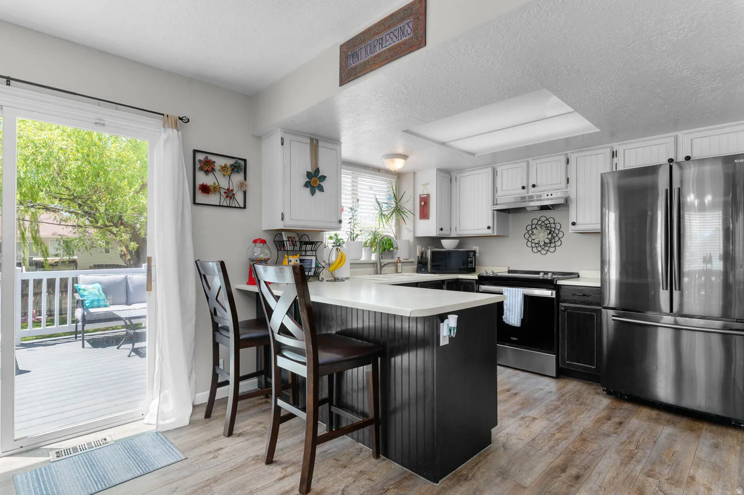 Kitchen featuring wood-finish flooring, white cabinetry, stainless steel appliances, and a central island with a light-toned countertop