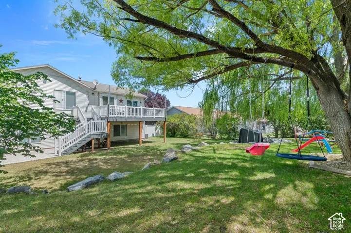 Spacious backyard featuring a multi-level deck with white railings, a lower-level concrete patio, a mature shade tree, and a grassy lawn
