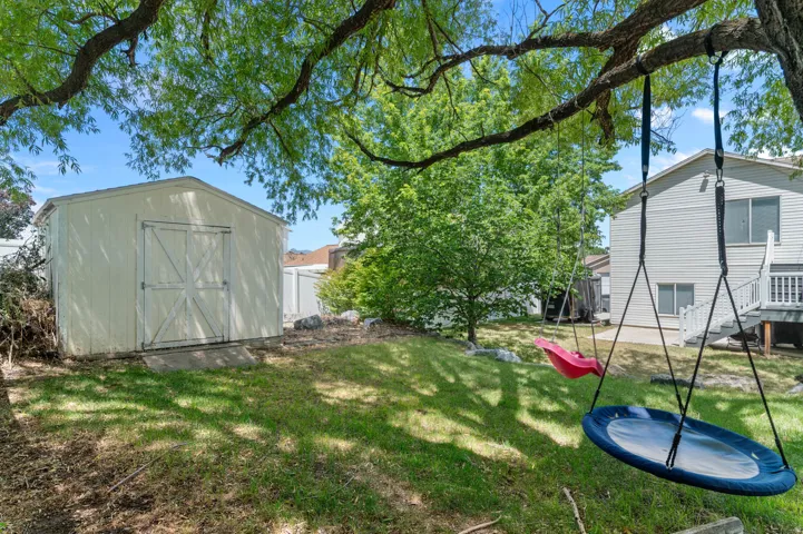 Expansive backyard featuring a lush lawn, mature trees, and a detached storage shed with double doors