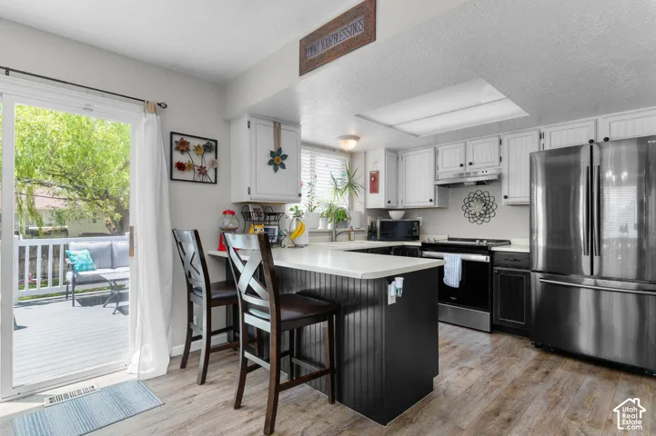 Kitchen featuring wood-finish flooring, white cabinetry, stainless steel appliances, and a central island with a light-toned countertop