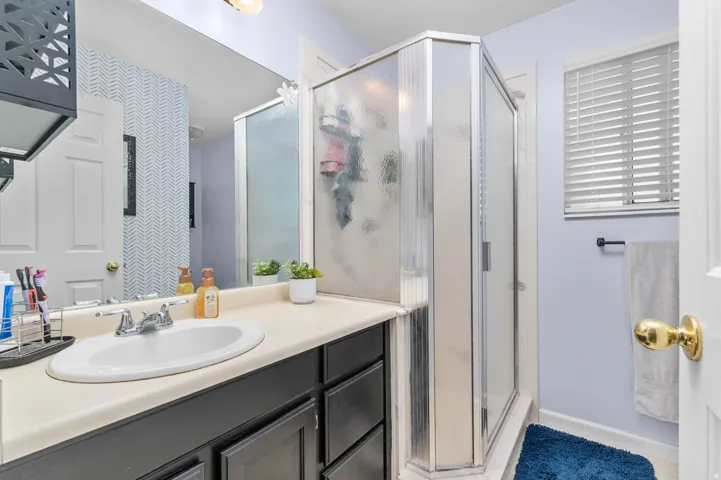 Bathroom featuring an integrated vanity sink with chrome faucet, dark wood-finish cabinetry, and a framed glass shower enclosure