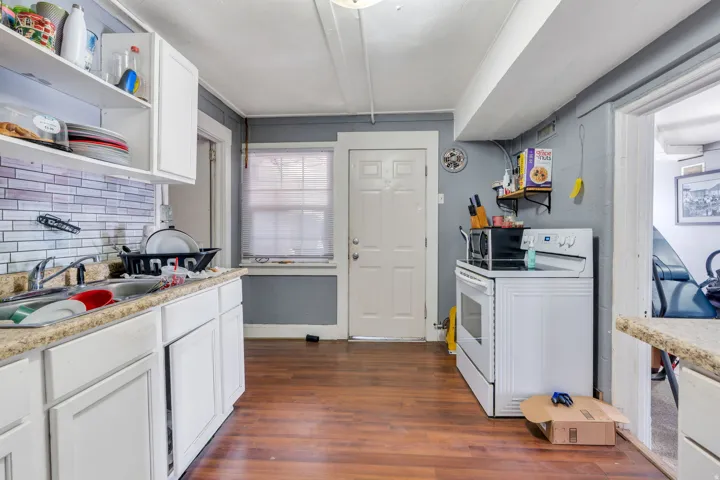 Rental: Kitchen featuring wood-finish flooring, white cabinetry, a tiled backsplash, and a window for natural light