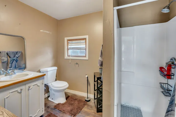 Bathroom featuring a single vanity, white toilet, and a stand-up shower with white surround