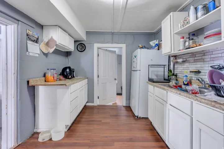 Rental: Kitchen featuring wood-finish flooring, white cabinetry, granite-look countertops, and a white tile backsplash
