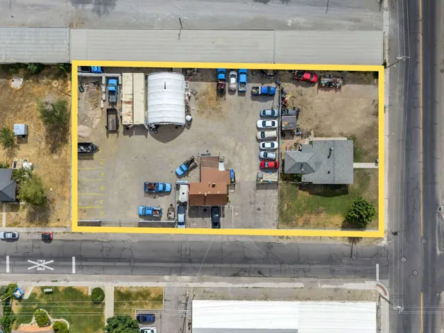 Expansive commercial property featuring a paved parking lot with marked spaces, multiple buildings including a residential-style structure, and a large covered storage area