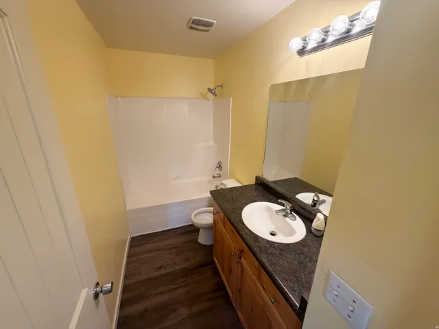 Bathroom featuring a white bathtub/shower combination, a vanity with a dark countertop and integrated sink, a large wall-mounted mirror, and wood-finish flooring