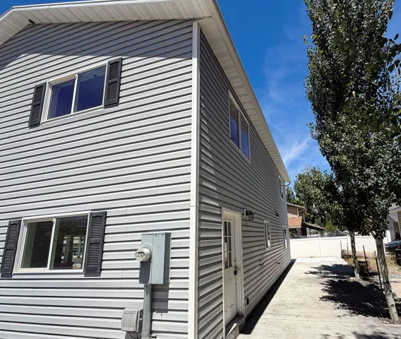 Two-story property featuring light gray horizontal siding, white trim, and dark louvered shutters