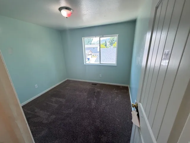 Bedroom featuring light blue walls, brown carpeting, a window with white trim, and a white paneled door