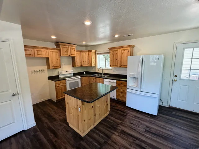 Kitchen featuring a central island with a dark countertop, wood-finish cabinetry, dark countertops, built-in range, and wood-finish flooring