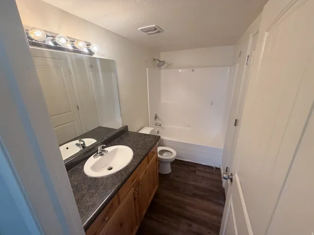 Bathroom with a wood-finish vanity, dual oval sinks, a dark speckled countertop, and a large mirror with a four-bulb vanity light