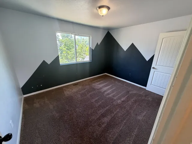 Interior room featuring a window with exterior tree views, carpet flooring, a flush-mount ceiling light fixture, and a paneled interior door