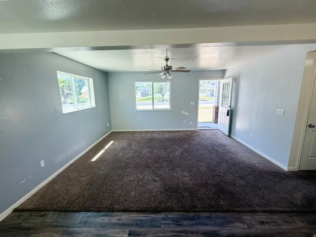 Spacious living area featuring neutral-toned walls, abundant natural light from multiple windows, and a ceiling fan with light fixture