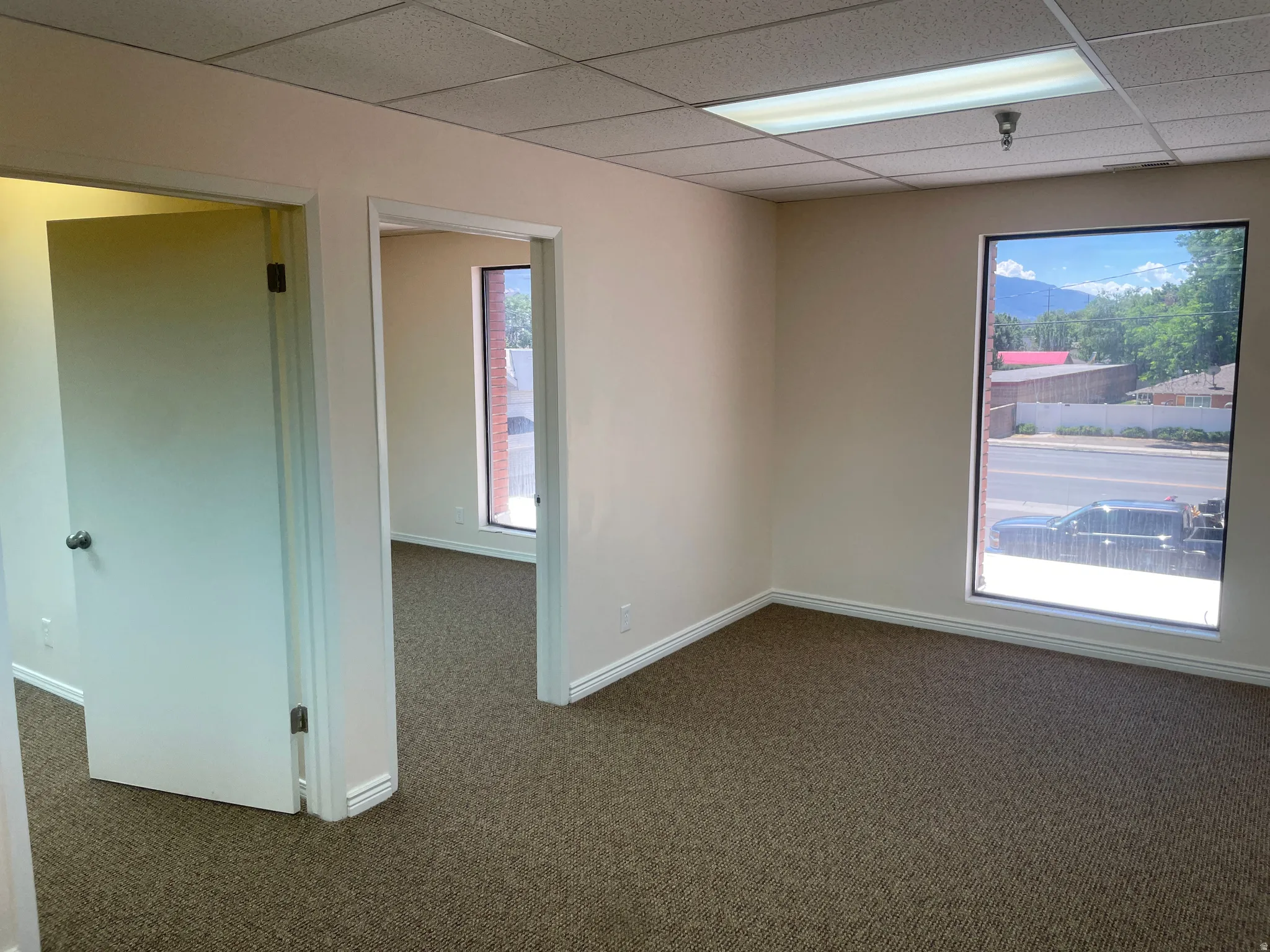 Spacious room featuring neutral walls, dark patterned carpet, and multiple windows