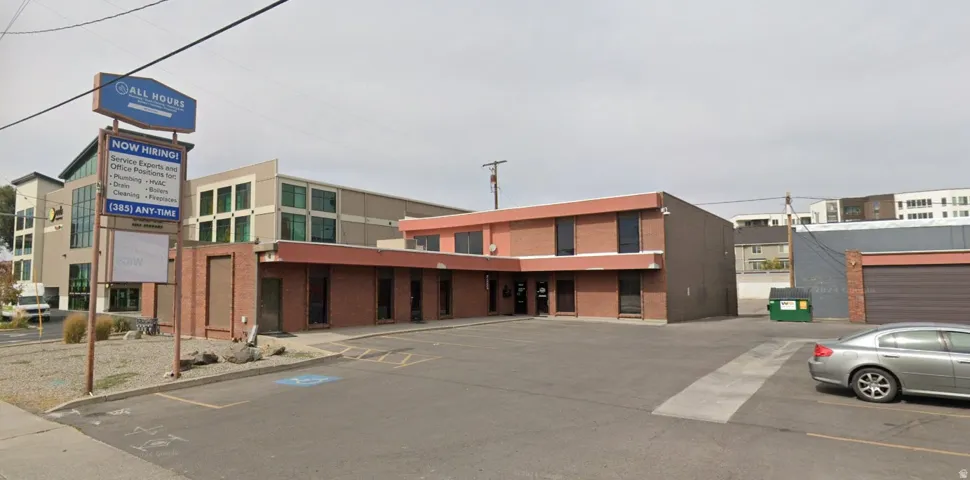 Brick-clad commercial building with multiple large windows, a flat roof, and an asphalt parking area