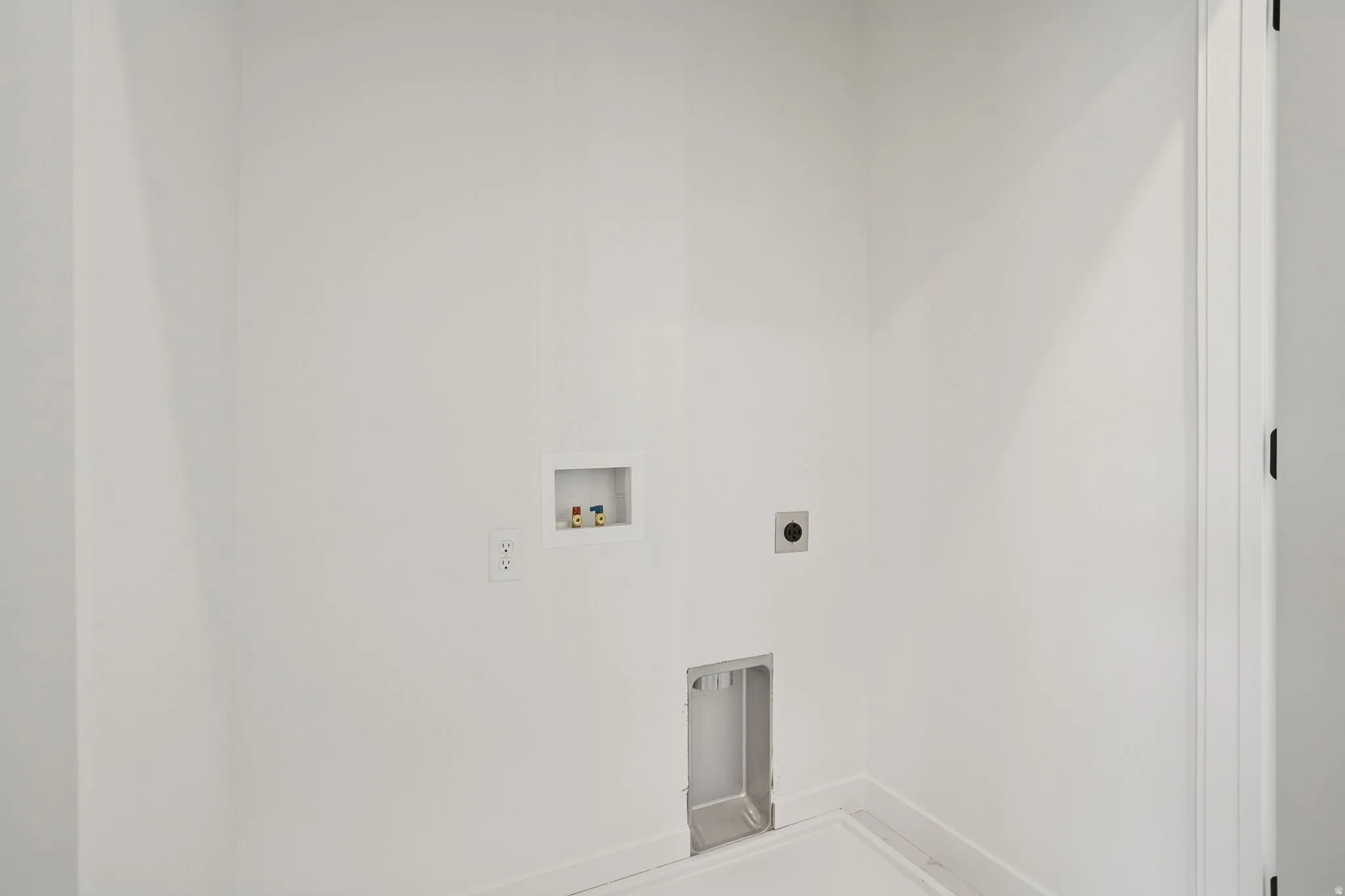 Dedicated laundry area featuring clean white walls, a built-in water supply box, and a floor drain for convenience