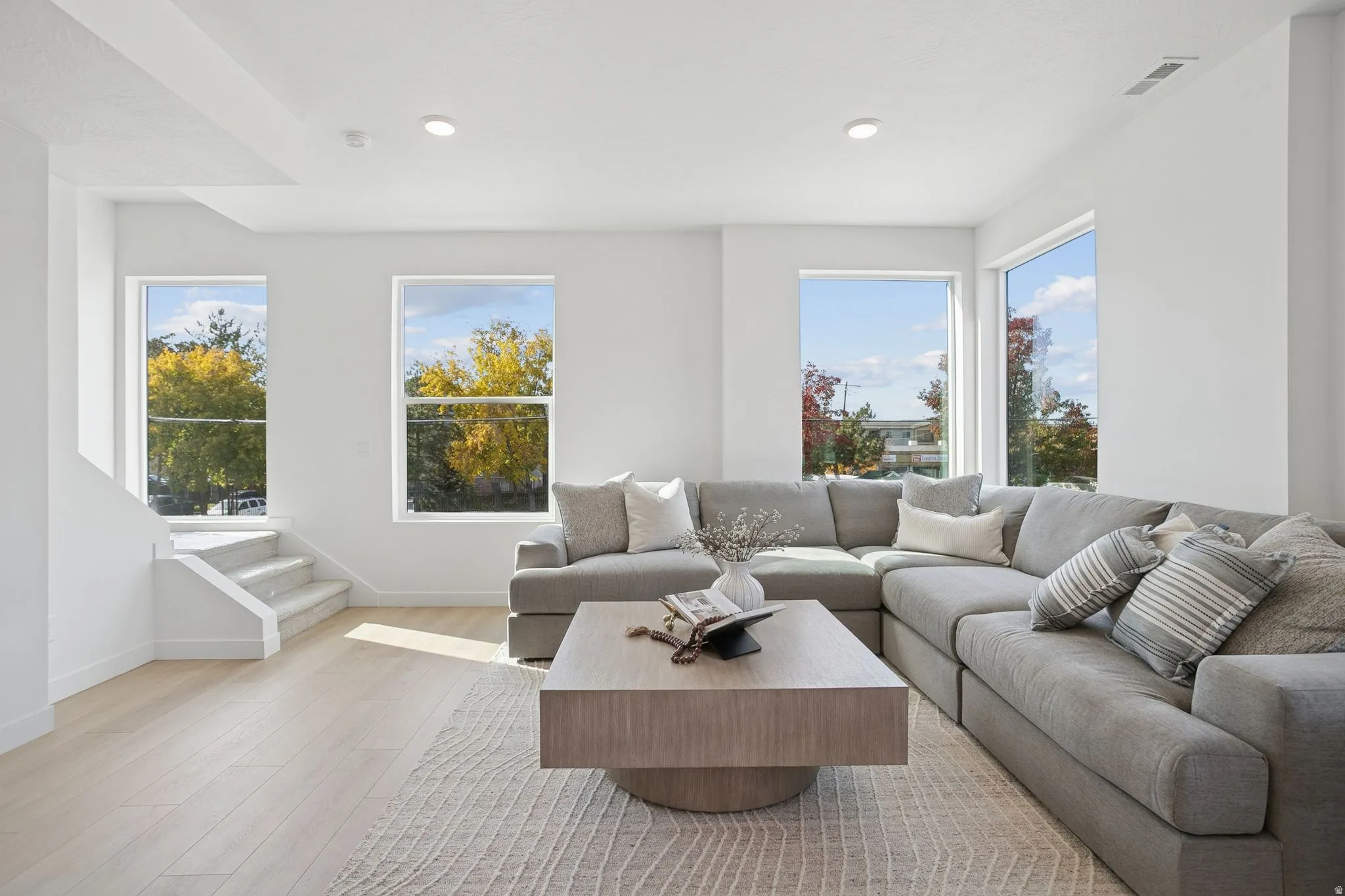 Spacious room featuring multiple windows, recessed lighting, light wood-finish flooring, and carpeted stairs