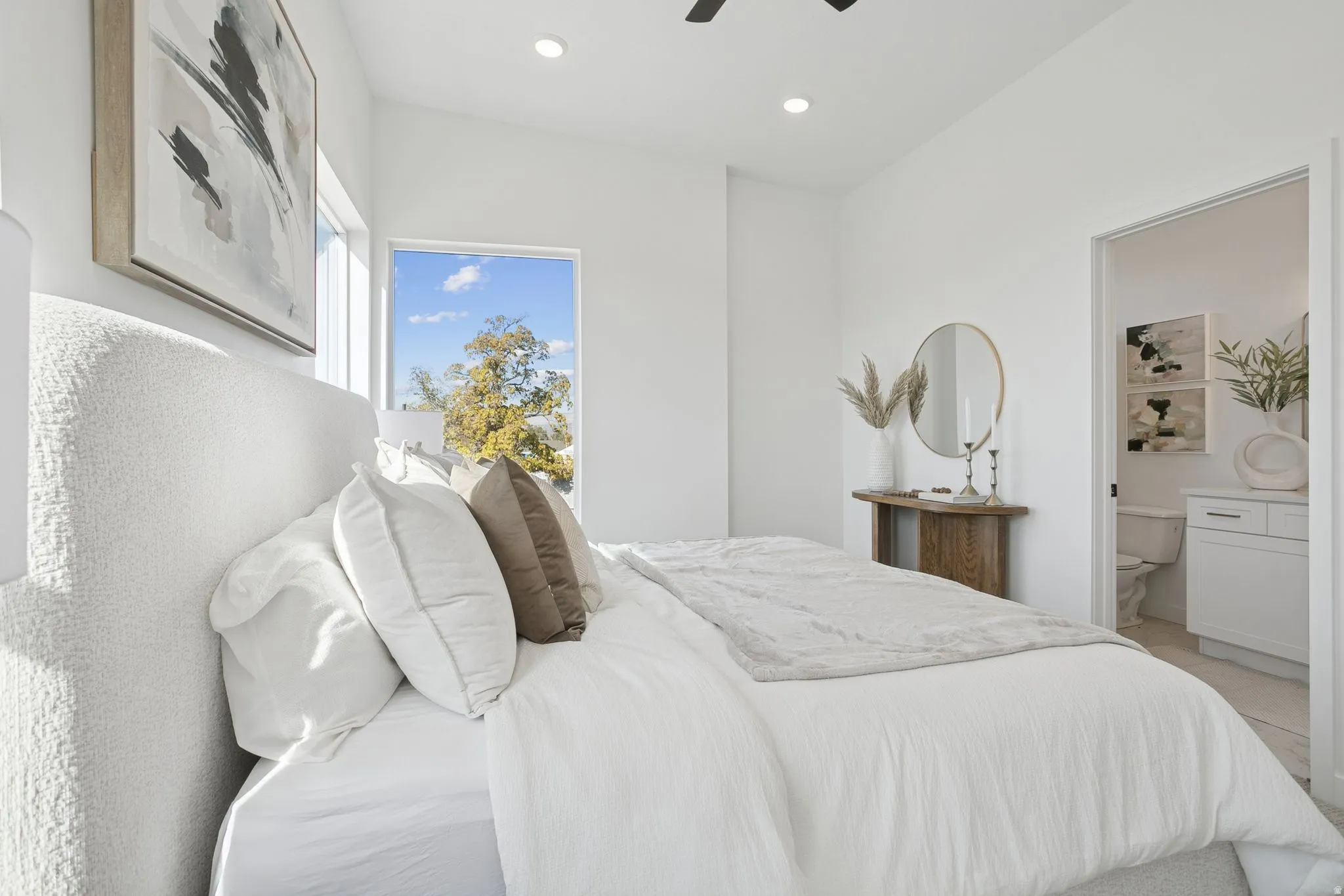 Bright interior space featuring a recessed light fixture, a window with exterior tree line, and an open doorway revealing a bathroom with a white vanity and toilet