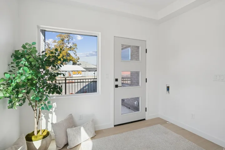 Entryway featuring a white door with three glass inserts, a large window, light wood-finish flooring, white baseboards, and bright white walls