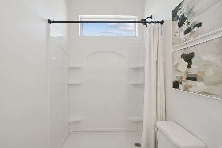 Walk-in shower with integrated shelving, a high transom window, and a dark bronze shower rod