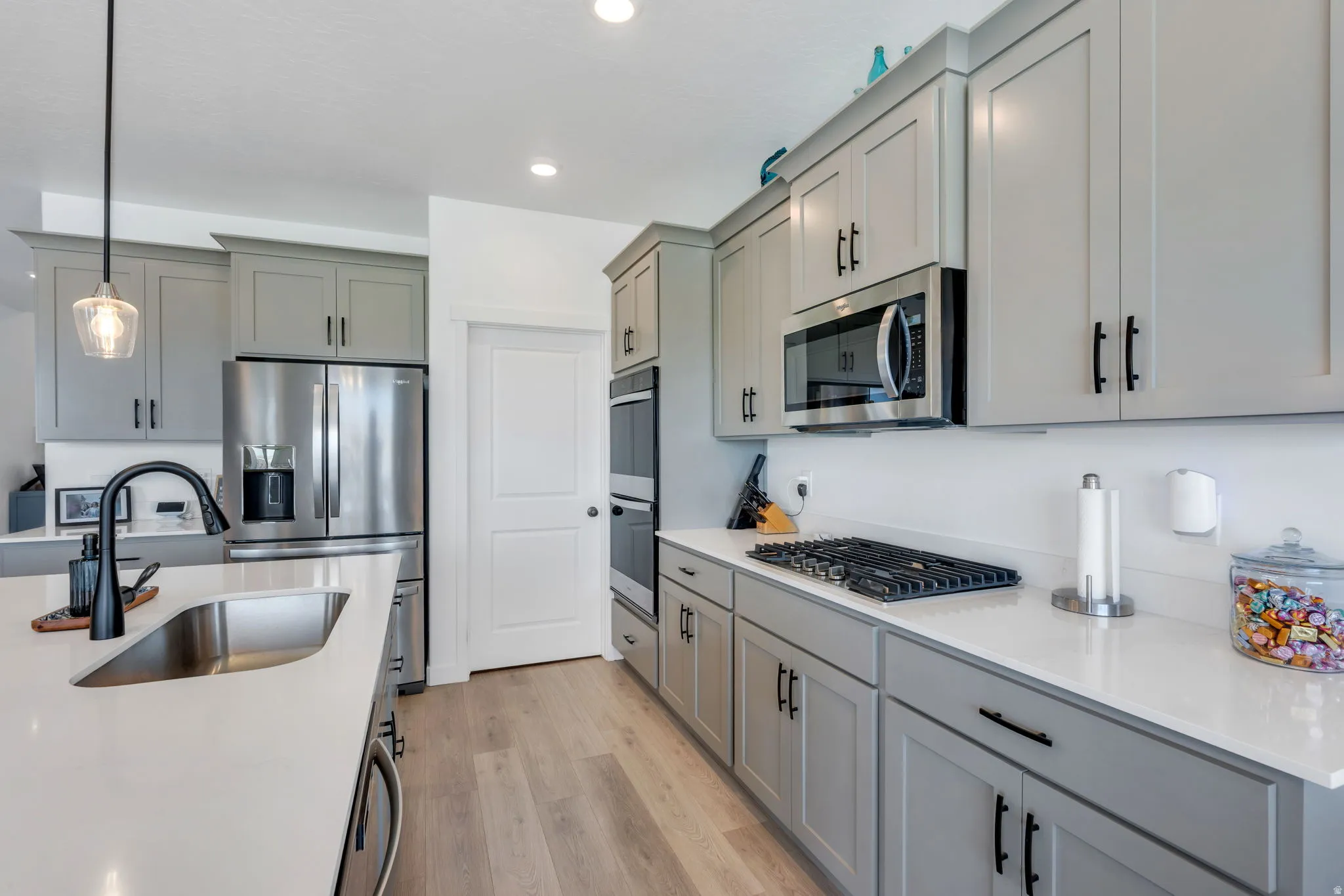 Contemporary kitchen featuring light gray cabinetry, stainless steel appliances, quartz countertops, wood-finish flooring, and a large kitchen island with an undermount sink
