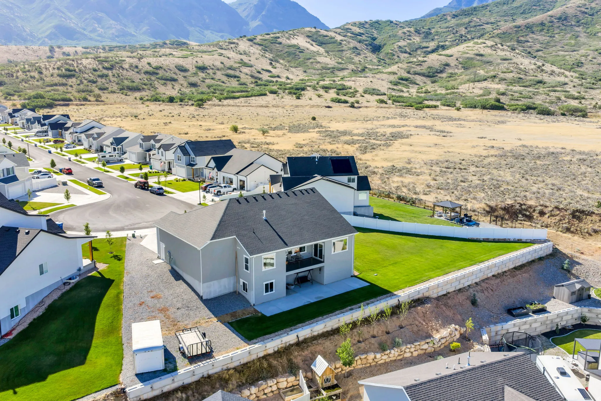Modern residential property with a light gray exterior, dark shingle roof, and a private backyard featuring a manicured lawn