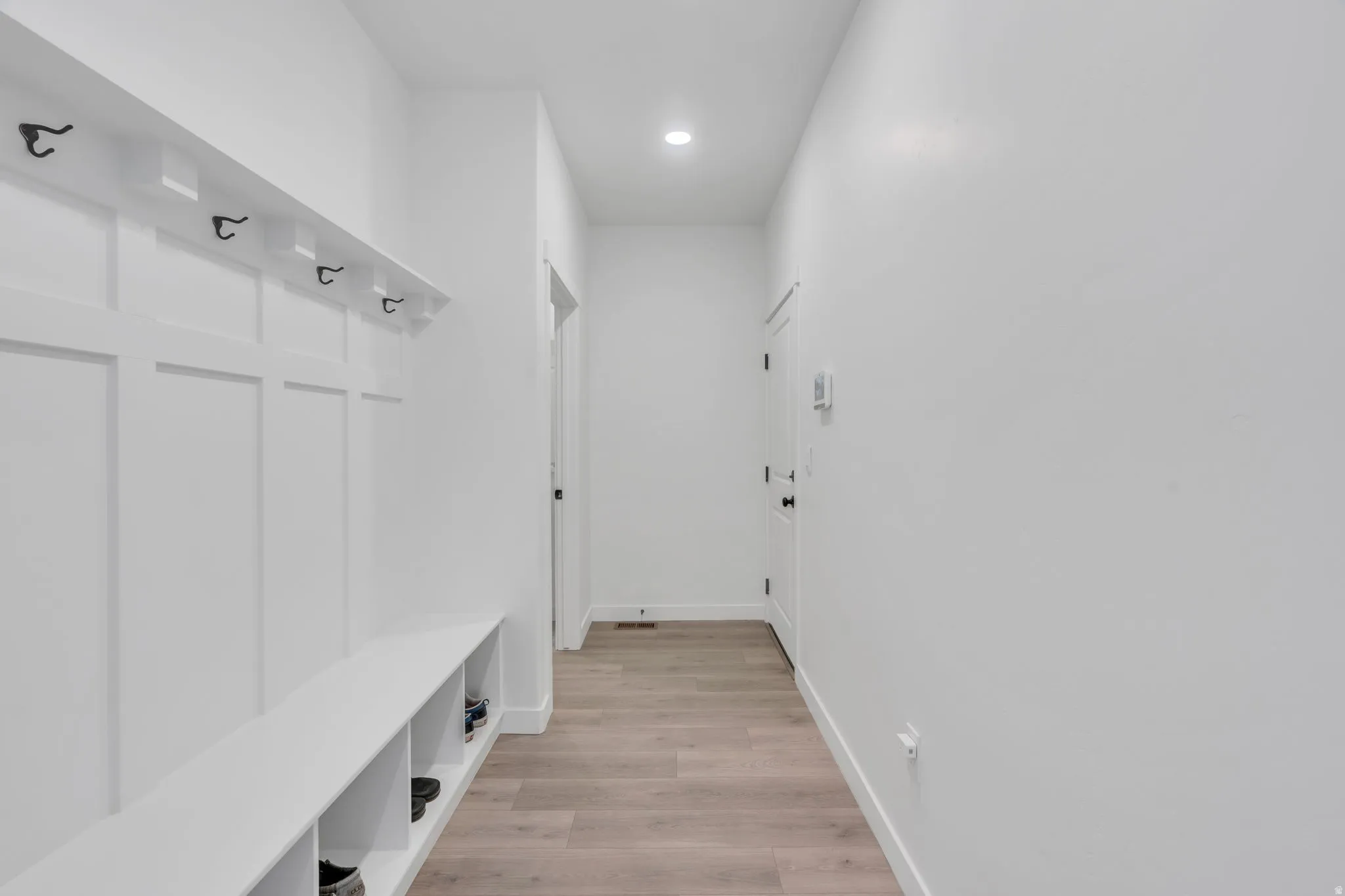 Entryway featuring board and batten wall treatment, integrated bench seating with open storage, and a row of black coat hooks