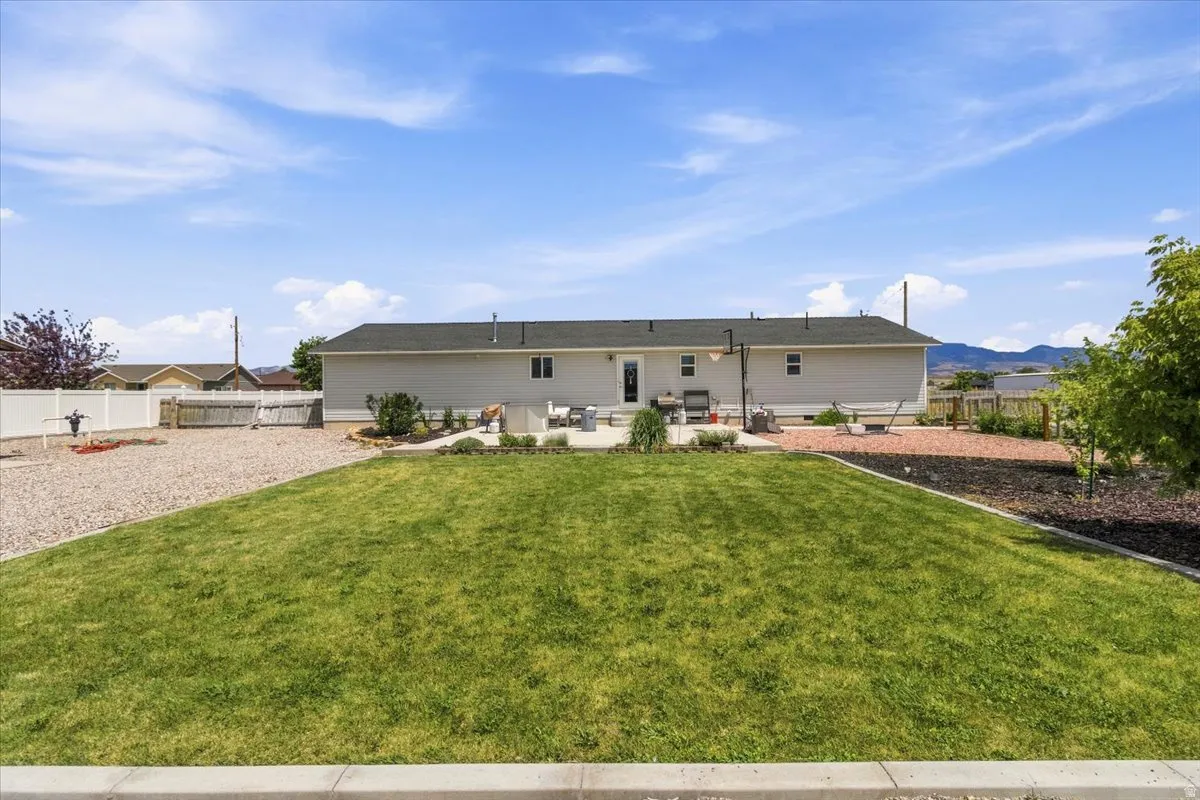 Expansive rear yard featuring a large grass lawn, a white vinyl privacy fence, and a gravel area