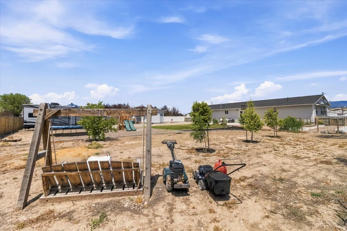 Spacious rear yard featuring a wooden swing structure, young trees, and a visible trampoline