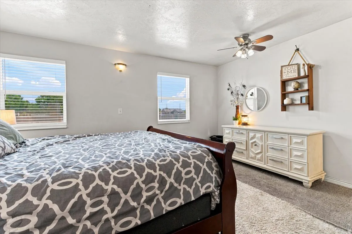 Bedroom featuring two windows with horizontal blinds, a ceiling fan with light fixture, and a wall-mounted light fixture