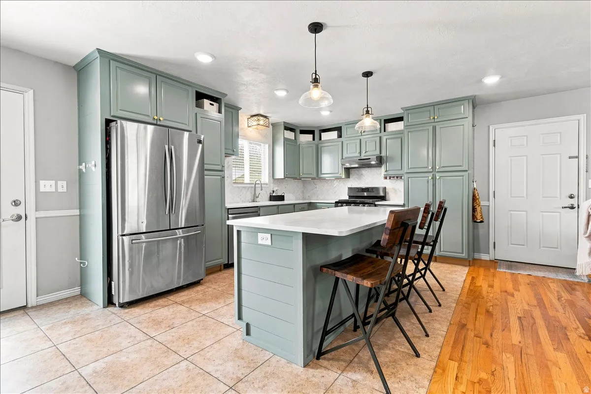 Spacious kitchen featuring sage green cabinetry, stainless steel appliances, a center island with countertop seating, recessed lighting, and pendant fixtures