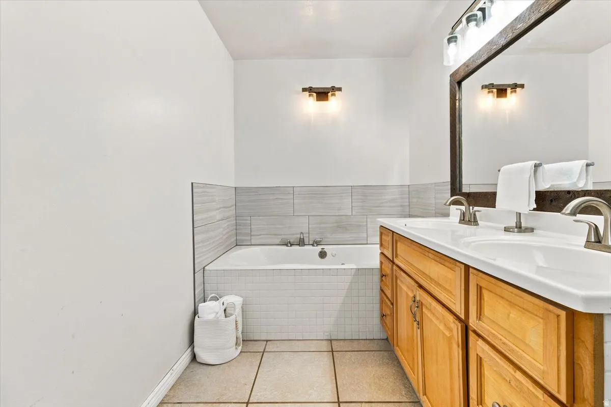 Bathroom featuring a built-in tub with white subway tile surround, light wood vanity with dual sinks, brushed nickel faucets, and a large wood-framed mirror