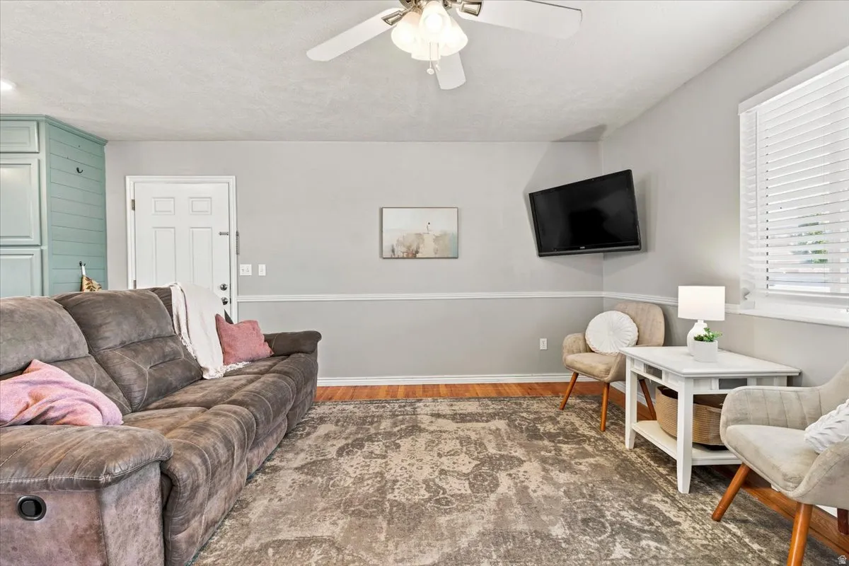 Bright living area featuring wood-finish flooring, a ceiling fan, window blinds, and a two-tone wall finish