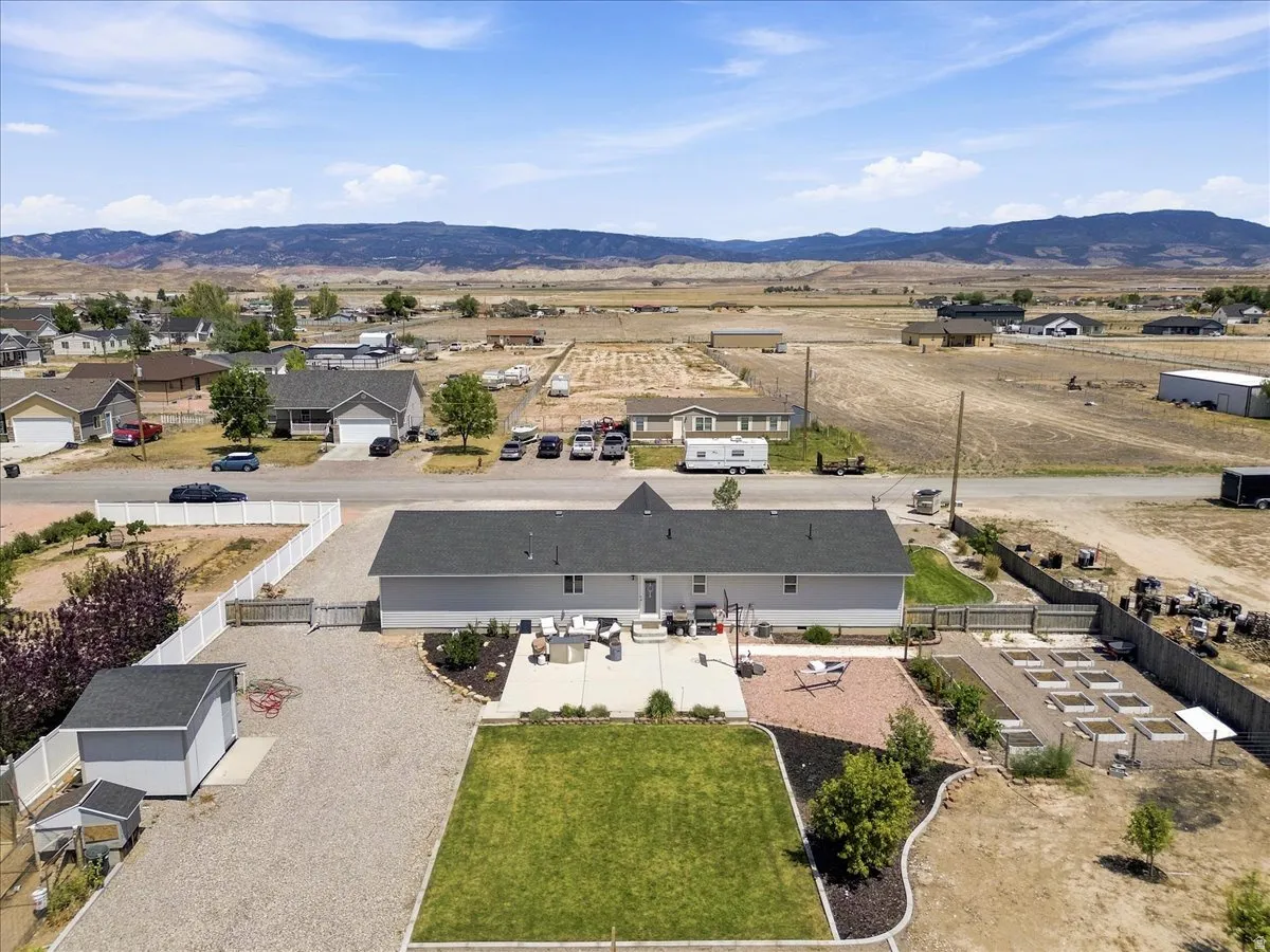 Expansive outdoor area featuring a dedicated garden with raised beds, a well-maintained lawn, a spacious concrete patio, a gravel hardscape, and a storage shed
