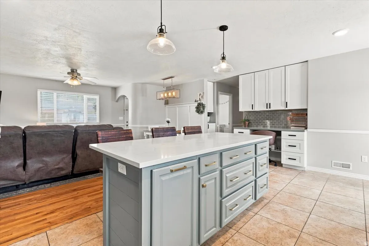 Kitchen island with light-toned countertop, pendant lighting, and ample cabinetry
