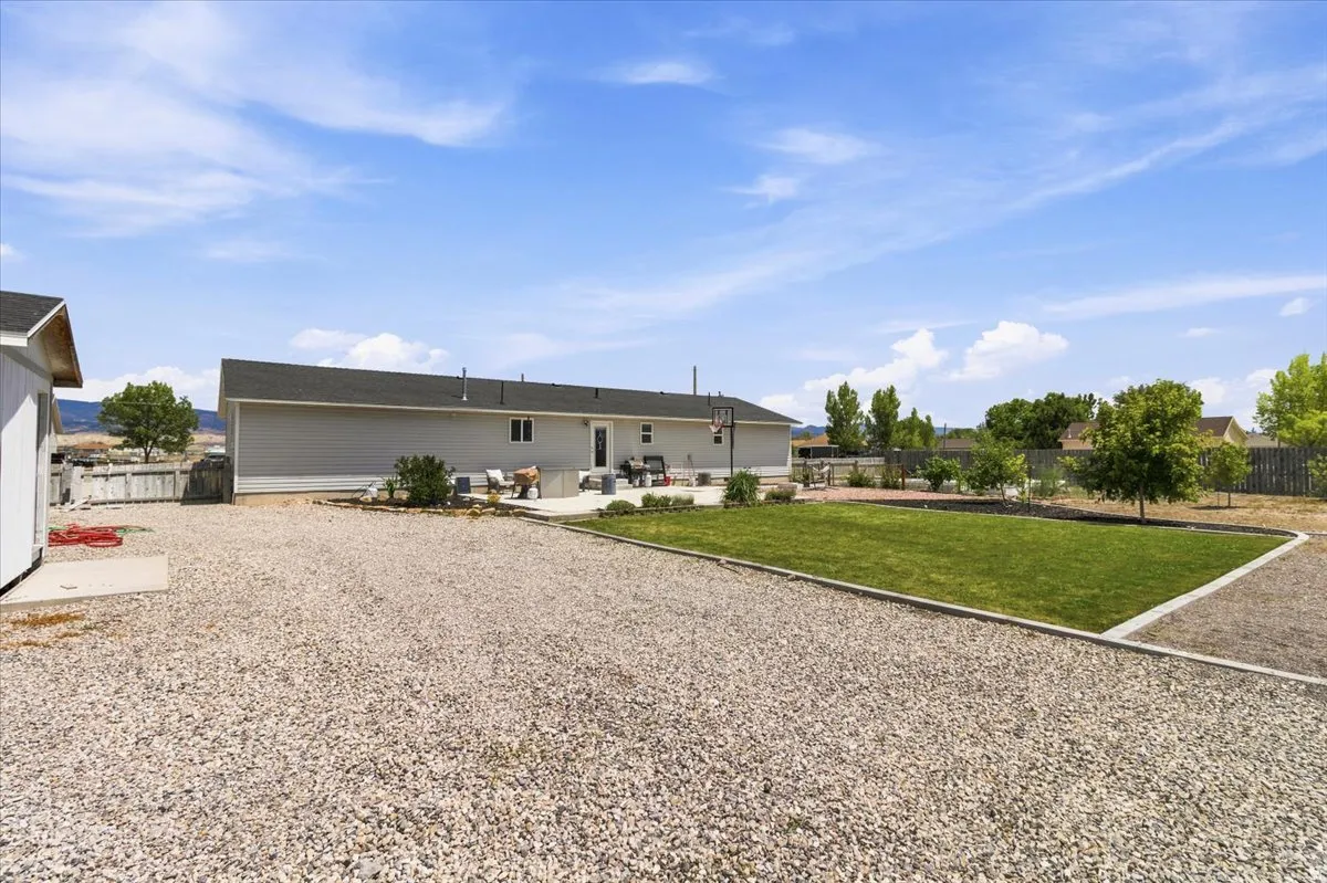 Expansive gravel yard featuring a detached shed, a manicured lawn area, a paved patio, and mature trees
