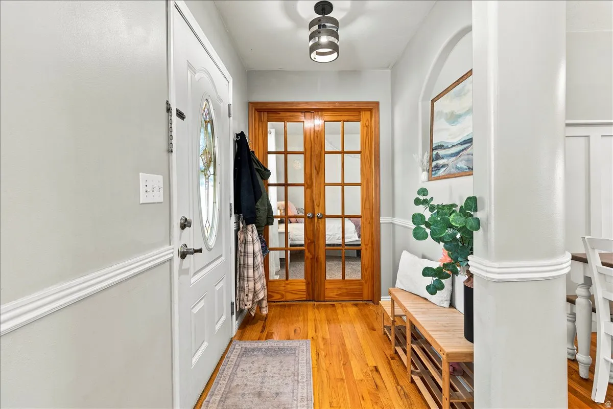 Entryway featuring wood-finish flooring, a white paneled entry door with an oval stained glass insert, and natural wood French doors
