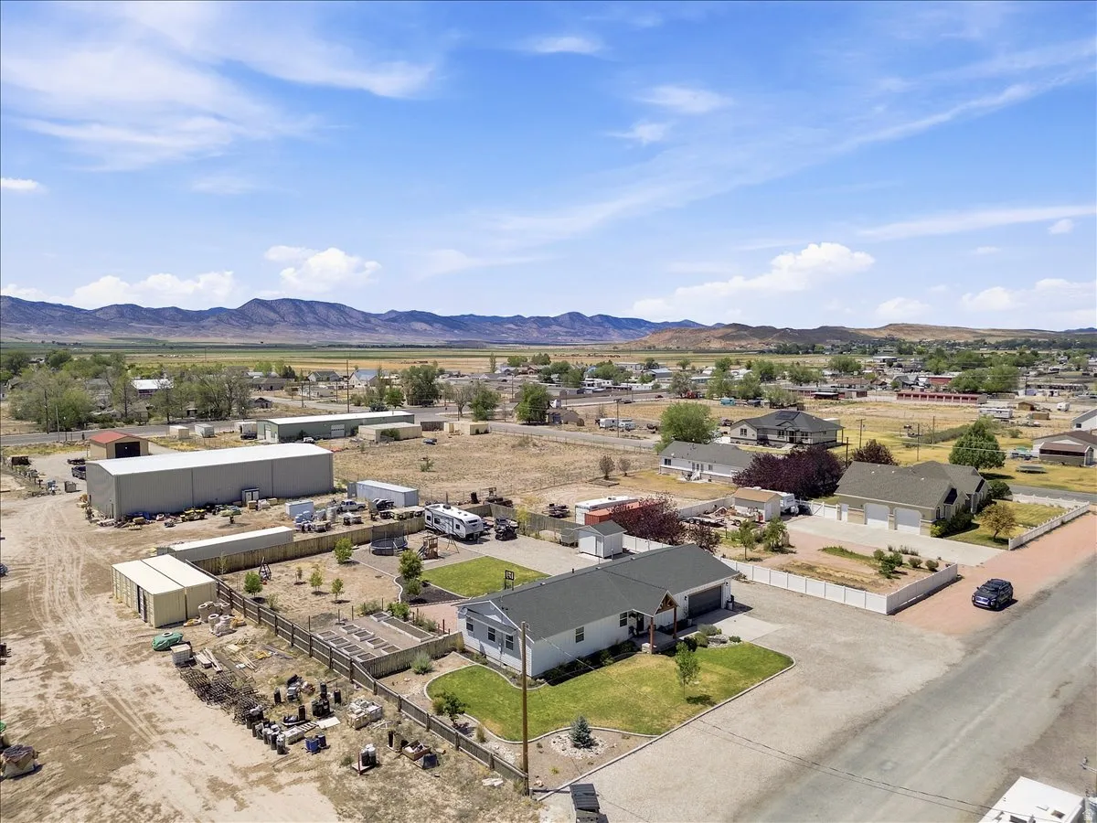 Aerial perspective showcasing a property featuring a single-story residence with an attached garage, a gravel driveway, and a fenced perimeter