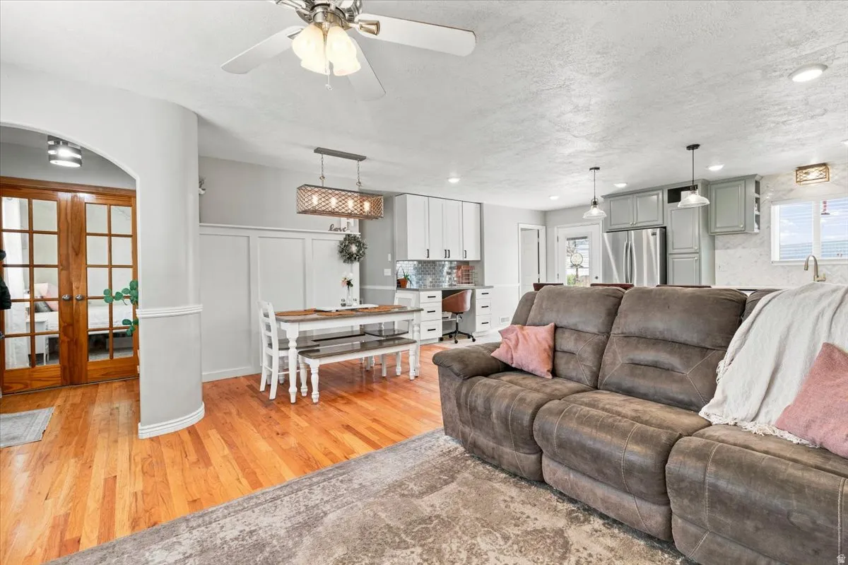 Open-concept interior featuring wood-finish flooring, a kitchen with light-toned cabinetry and stainless steel appliances, and an arched entryway with French doors