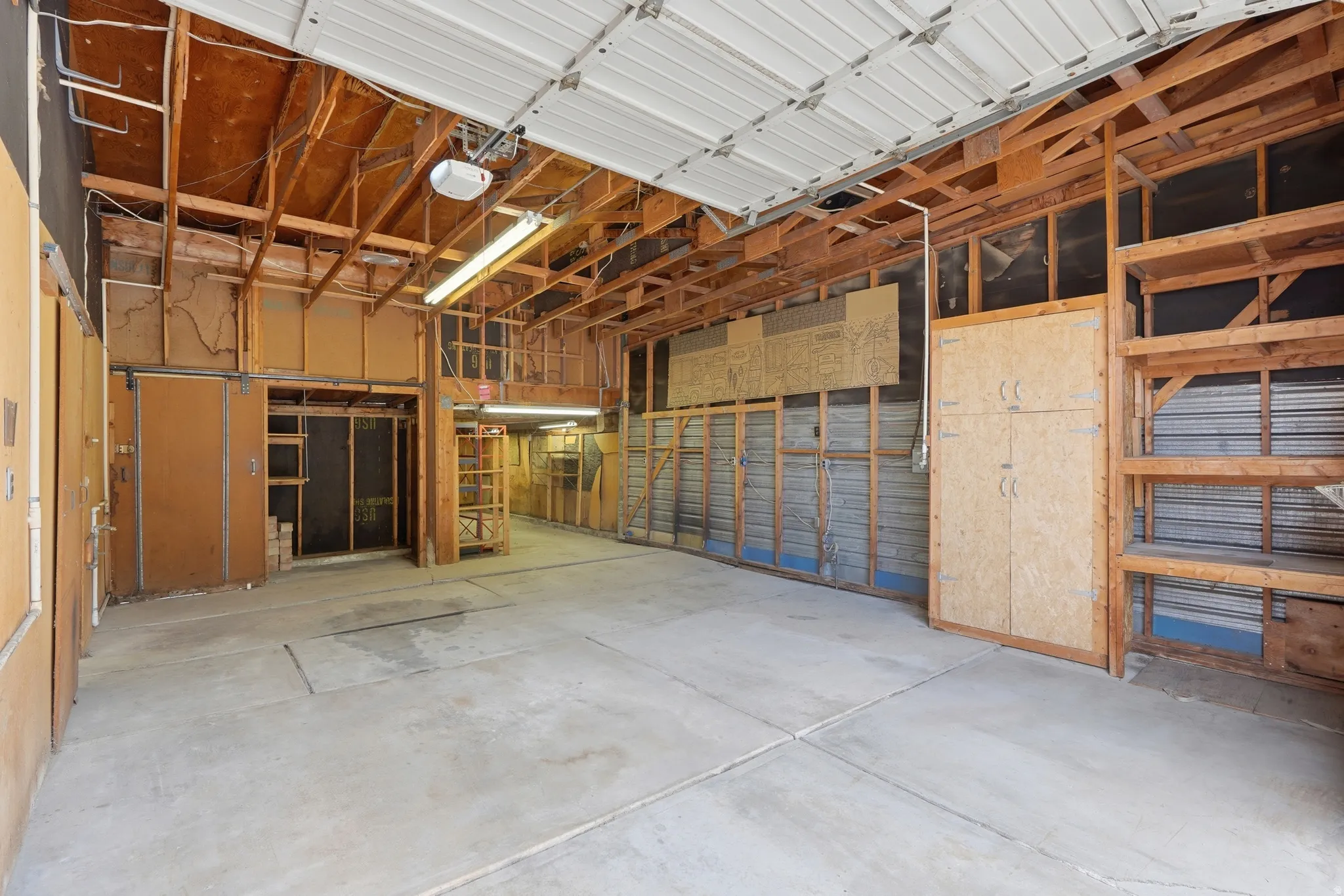 Spacious garage featuring a concrete floor, exposed wood framing, and a white overhead door