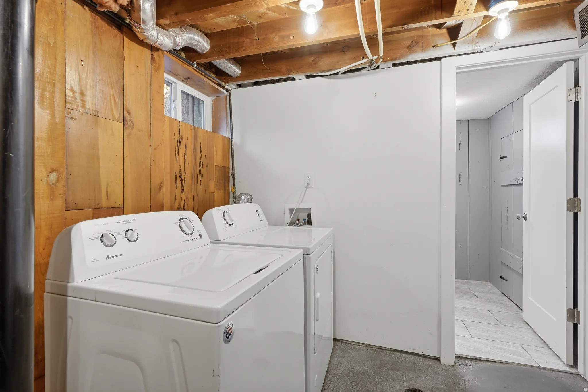 Utility area featuring exposed wood ceiling joists, wood-paneled wall, a small window, and concrete flooring
